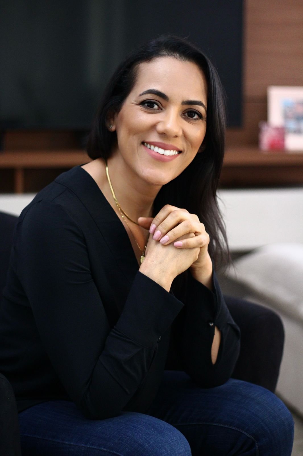 Cecília sentada no sofá, sorrindo, em um momento descontraído